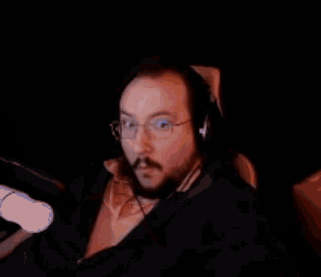 a man with glasses and a mustache is wearing headphones and making a face .