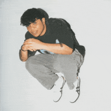 a man in a black shirt and grey jeans is sitting on the floor