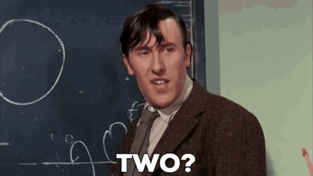 a man in a suit and tie is standing in front of a blackboard with the word two written on it