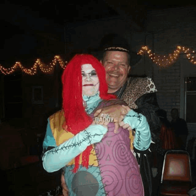 a man and a woman in costumes are posing for a picture . the woman is wearing a red wig .