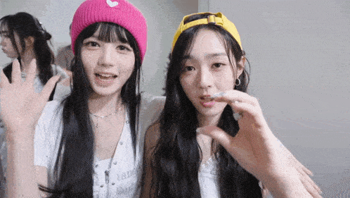 a girl wearing a pink hat with a heart on it is standing next to another girl wearing a yellow hat