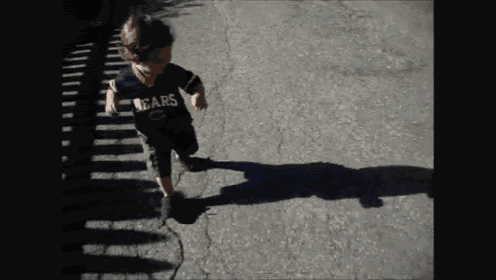 a young boy wearing a shirt that says " big " is walking down a street