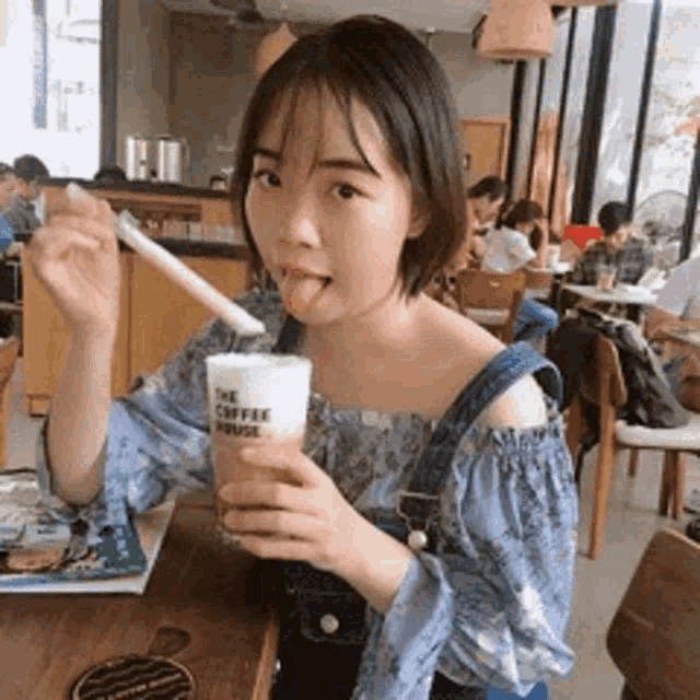 a woman is sitting at a table with a cup of coffee and a straw .