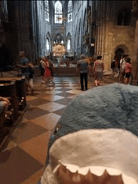 a stuffed shark is standing in a church with people walking in the background .