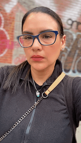 a woman wearing glasses and a necklace is taking a picture of herself