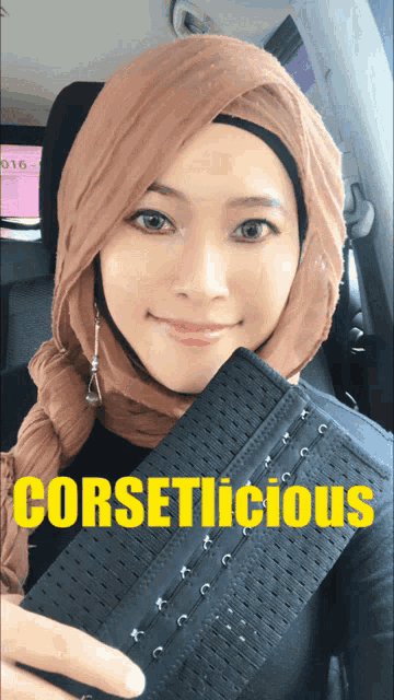 a woman wearing a hijab is holding a corset which says corsetlicious on it