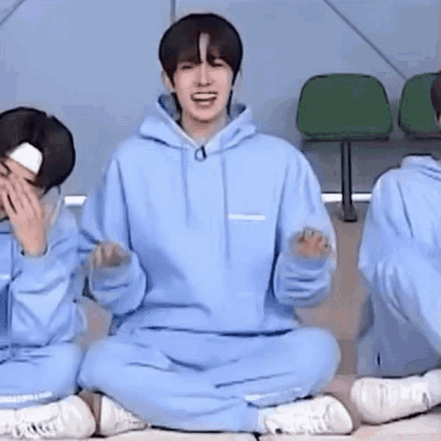 a boy in a blue hoodie is sitting on the floor with his legs crossed and laughing .