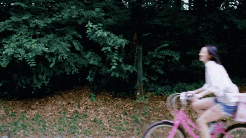 a woman is riding a pink bike down a path
