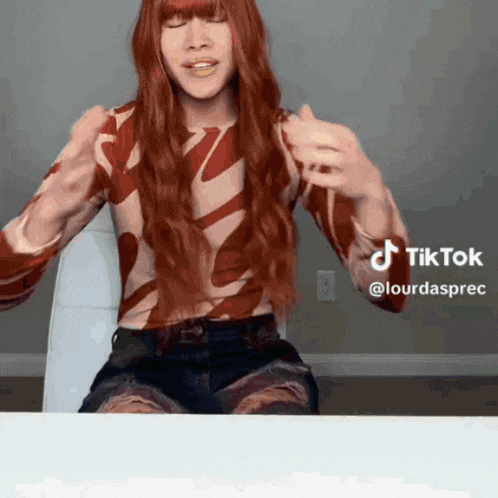 a woman with long red hair is sitting at a table with a tiktok watermark on the bottom