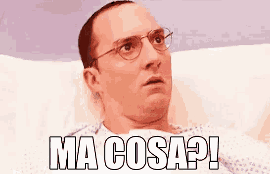 a man with glasses is laying in a hospital bed with the words `` ma cosa ? '' above him .