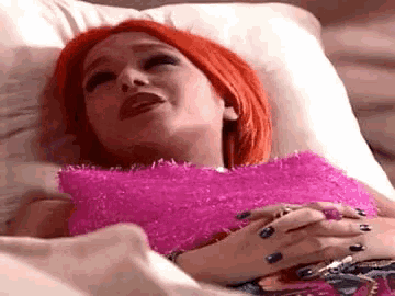 a woman with red hair is laying in a hospital bed wearing a pink top .