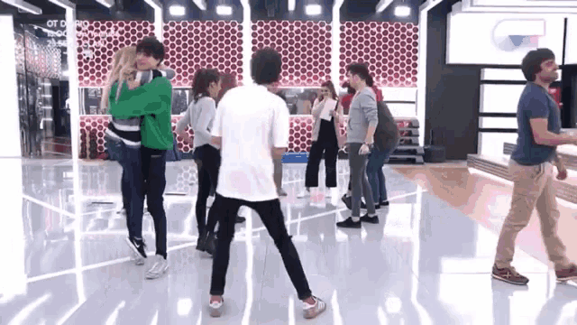 a group of people are dancing in a room with a man in a blue shirt walking behind them