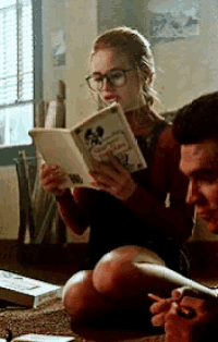 a woman sitting on the floor reading a book with a man sitting next to her smoking a cigarette