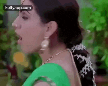 a close up of a woman 's face with her mouth open wearing a green saree and earrings .