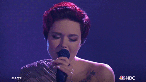 a woman singing into a microphone with the nbc logo on the bottom right