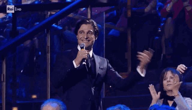 a man in a suit holds a microphone in front of a crowd and says rai 1 hd on the bottom