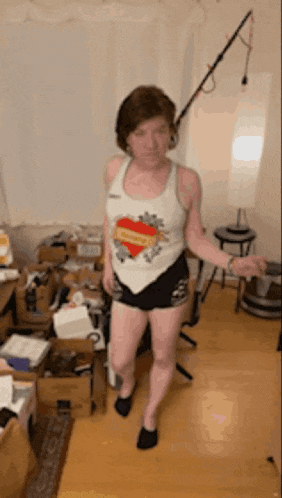 a woman in a tank top and shorts is standing in a messy room