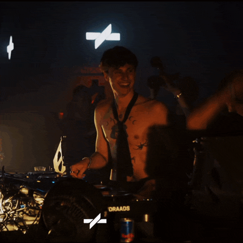 a shirtless man in a tie stands in front of a dj booth that says draado