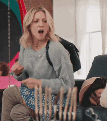 a woman in a gray sweater is sitting on a couch with her mouth open