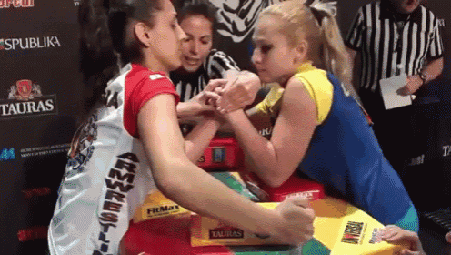 two women arm wrestling in front of a tauras advertisement