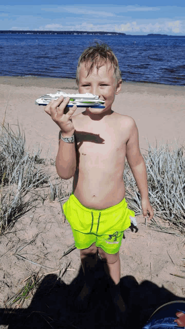 a young boy is holding a toy airplane in his mouth on the beach