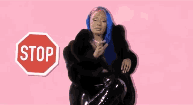 a girl with blue hair is sitting in front of a sign that says bad bitches can like anime too