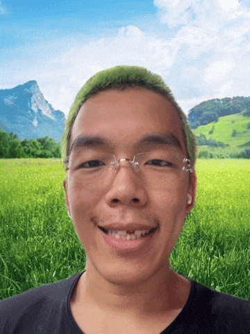a man with glasses and green hair smiles in front of a field