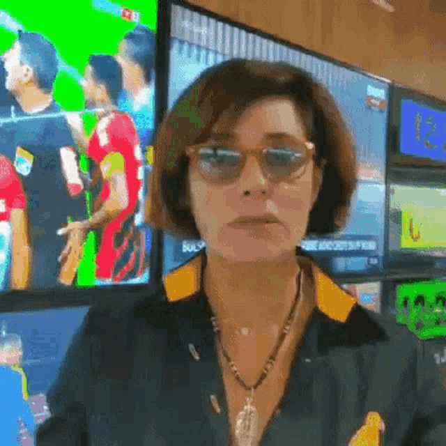 a woman wearing sunglasses and a necklace stands in front of a green screen with the number 12 on it