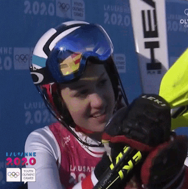 a woman wearing a helmet and goggles is holding a ski in front of a sign that says youth olympic games