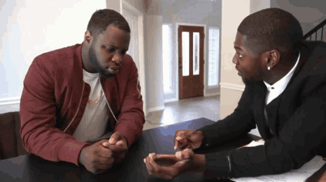 two men are sitting at a table looking at a phone