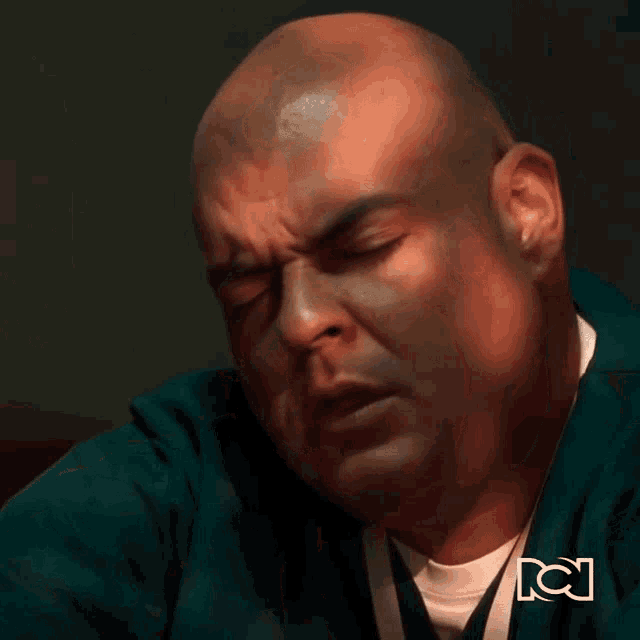 a bald man in a green jacket with the letter c on the bottom left
