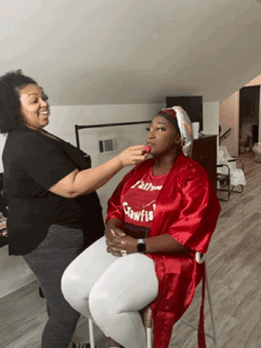 a woman is getting her makeup done by a woman wearing a red shirt that says claws