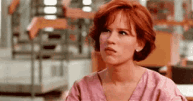 a woman with red hair is wearing a pink shirt .