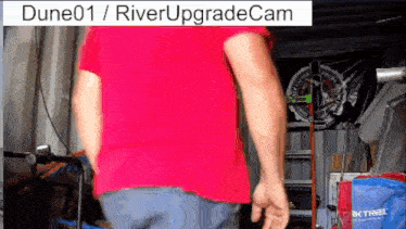a man in a red shirt is standing in front of a sign that says dune01 / river upgradecam