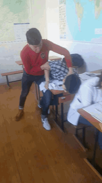 a boy in a red shirt is standing next to a boy in a plaid shirt in a classroom