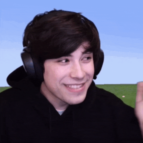 a young man wearing headphones and a black hoodie is smiling and looking at the camera .