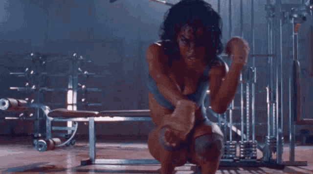 a woman is squatting down in a gym with her arms outstretched and a bench in the background .