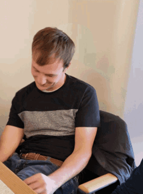a man in a black and grey shirt is sitting in a chair