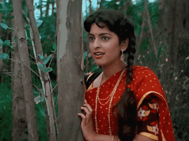 a woman in a red and yellow polka dot dress is standing next to a tree