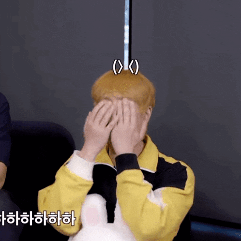 a man in a yellow jacket covering his face with his hands with korean writing on the bottom
