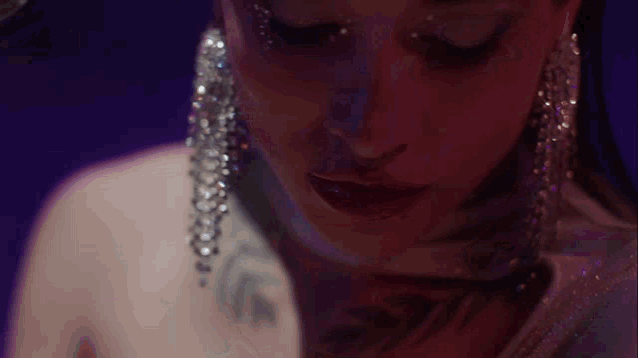 a close up of a woman 's face with earrings and a tattoo on her shoulder .