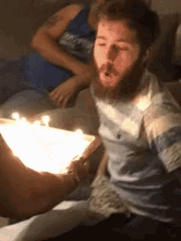 a man with a beard blows out candles on a birthday cake