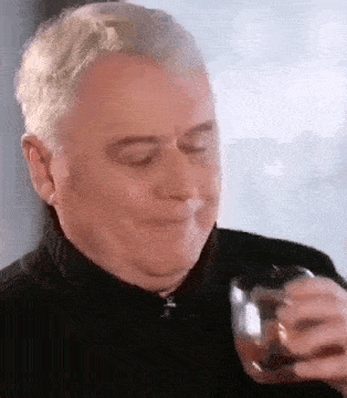 a man is holding a glass of whiskey in his hand and smiling .