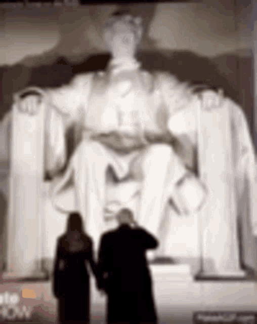 two people are standing in front of a statue of lincoln .