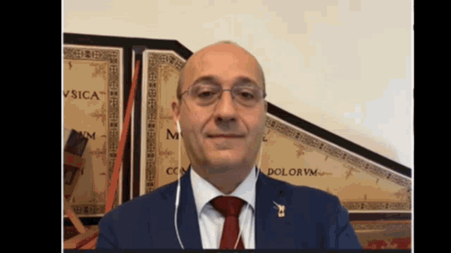a man wearing a suit and tie with the word dolorvm written on the wall behind him