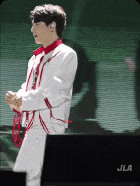 a man in a white jacket and red tie is standing in front of a screen that says jla on it
