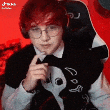 a young man with red hair and glasses is wearing headphones and a black and white sweater .