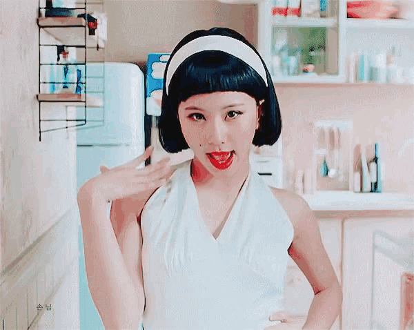 a woman in a white dress with a headband on her head is smiling in a kitchen .
