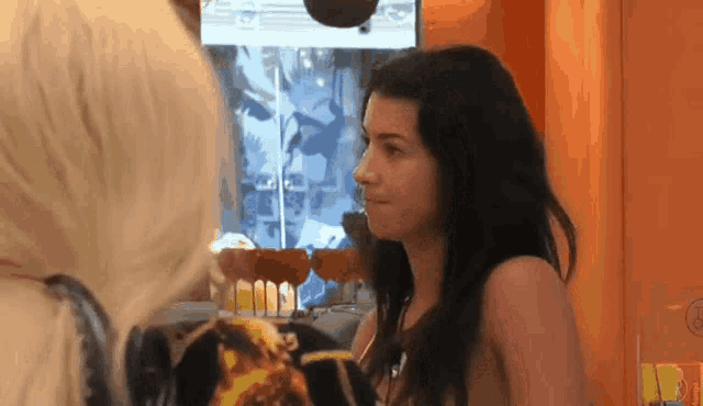 a woman looks at another woman in front of a screen that says ' a ' on it