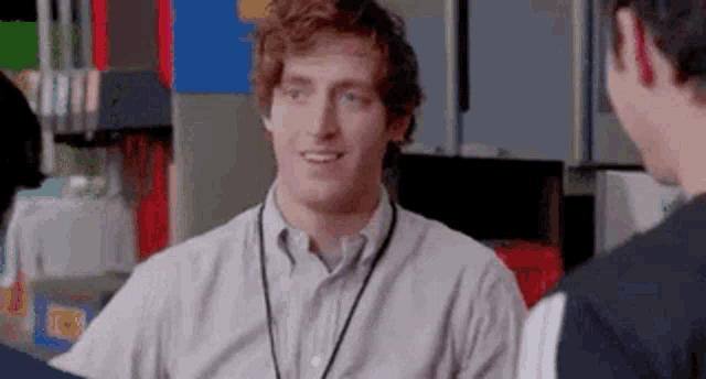 a man with a lanyard around his neck is smiling while talking to another man .